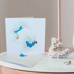 Faire-part papillons et aquarelle bleue posé sur une table d'appoint